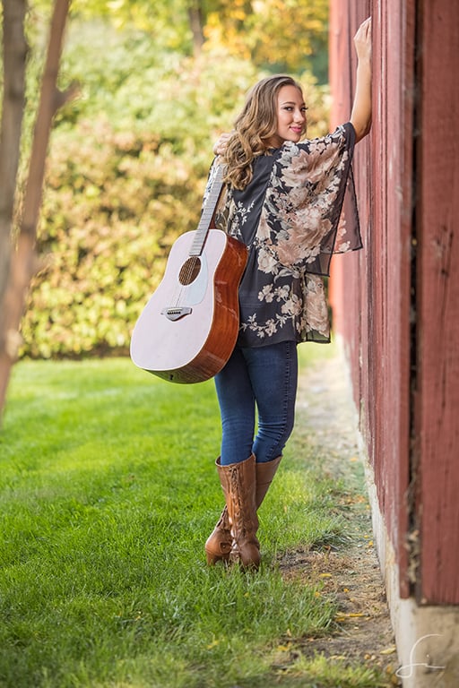 high school senior girl with guitar against red barn at hidden springs idaho