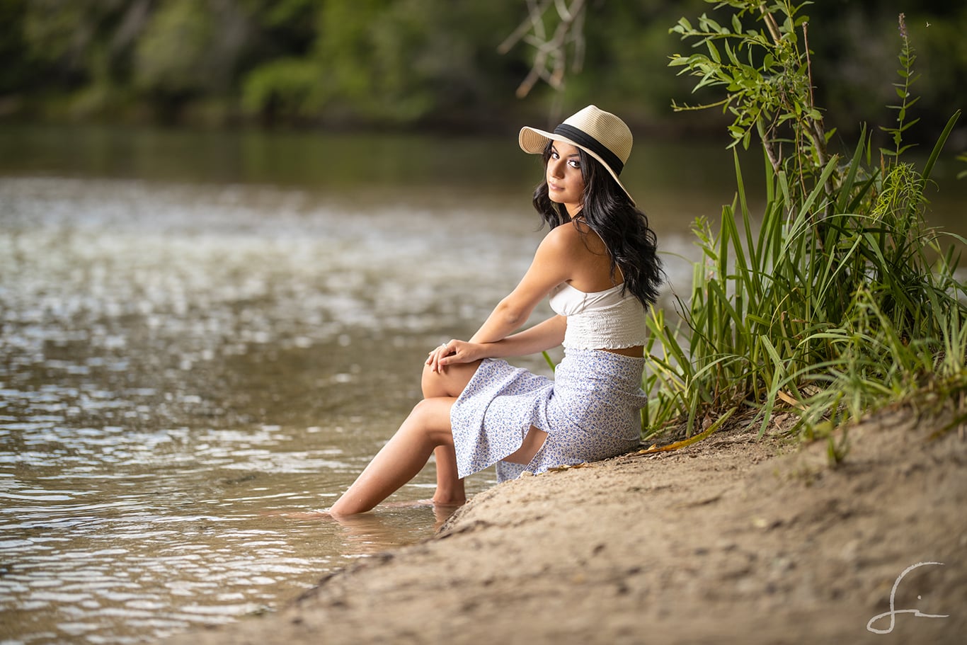 Senior High School girl sitting on the banks of the river with a summer outfit and a bolero hat
